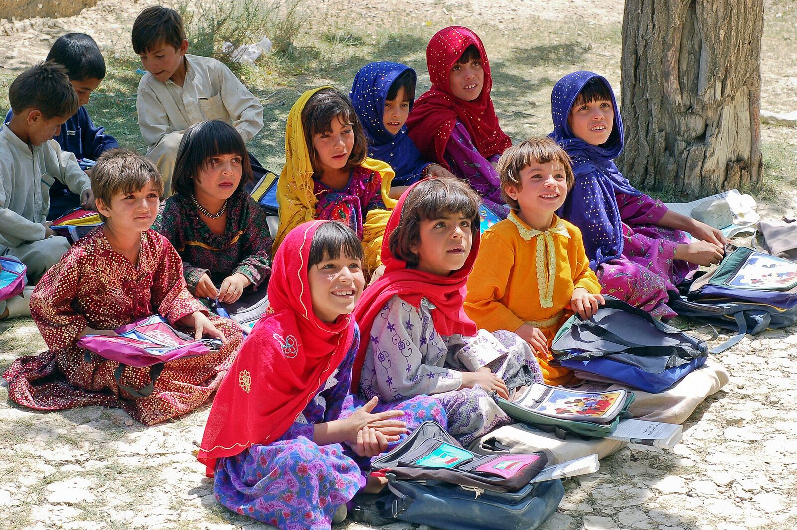 Afghan children learn outdoors with books, demonstrating the power of education and communication skills.